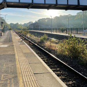 View along platform at train station, bridge and sun in background.