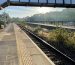 View along platform at train station, bridge and sun in background.