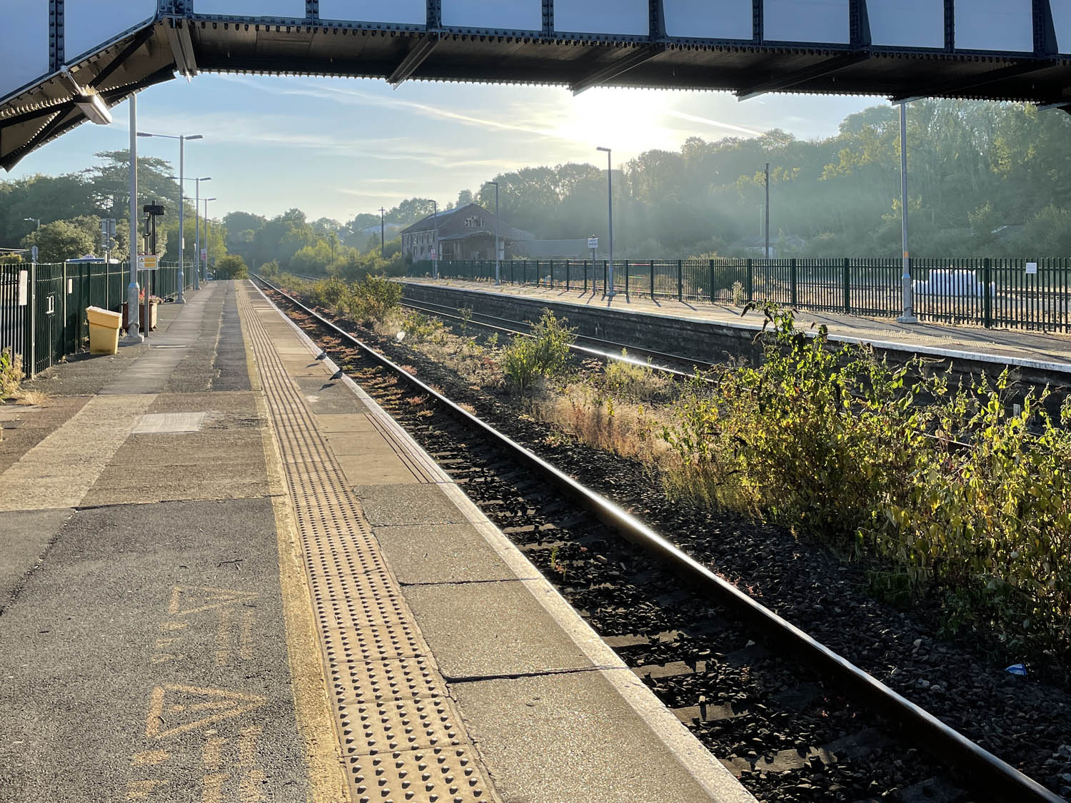 IMG_2109_1 View along platform at train station, bridge and sun in background.