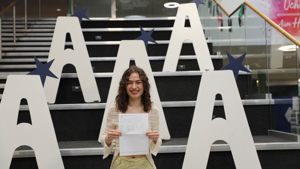 Madeleine holding results, large a's in background on stairs.