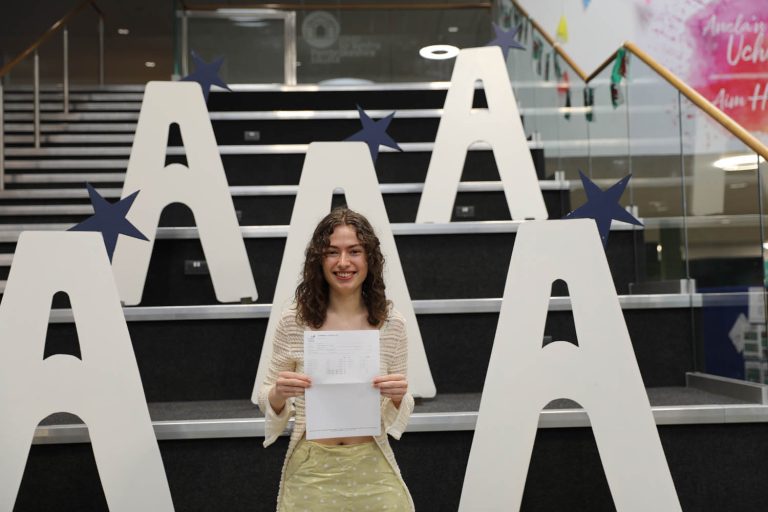 Madeleine holding results, large a's in background on stairs.