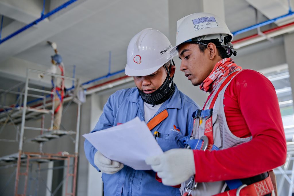 Two people in factory clothing with hard hats looking at paperwork.