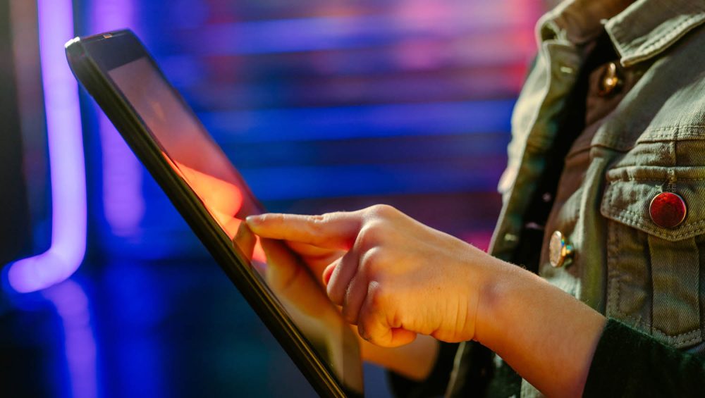 Close up of person using tablet standing on the colorful neon lights background.