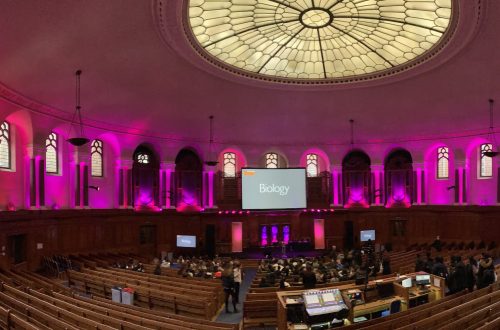 Inside the Emmanuel Centre, London. Pink lighting with rows of seats.