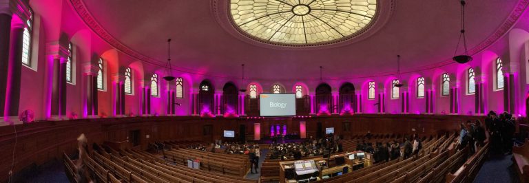 Inside the Emmanuel Centre, London. Pink lighting with rows of seats.