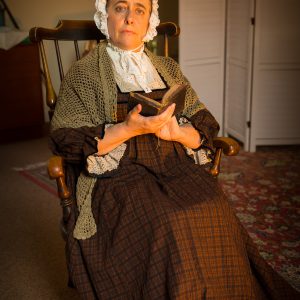 Older lady in traditional Welsh clothing on wooden rocking chair holding a book.