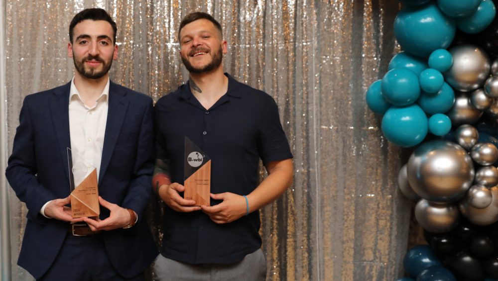 Haidar (left) and Daniel (right) holding their trophies in front of a silver sparkly background