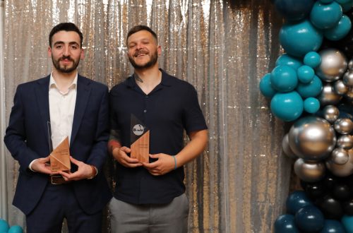 Haidar (left) and Daniel (right) holding their trophies in front of a silver sparkly background