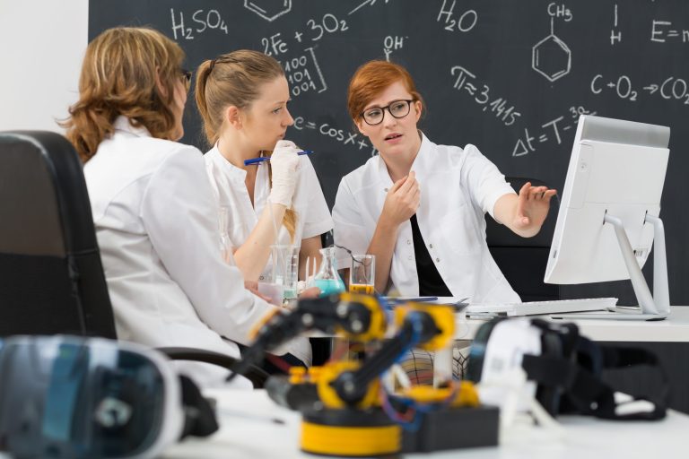 Three people in lab coats looking at a computer screen with science equipment around them.
