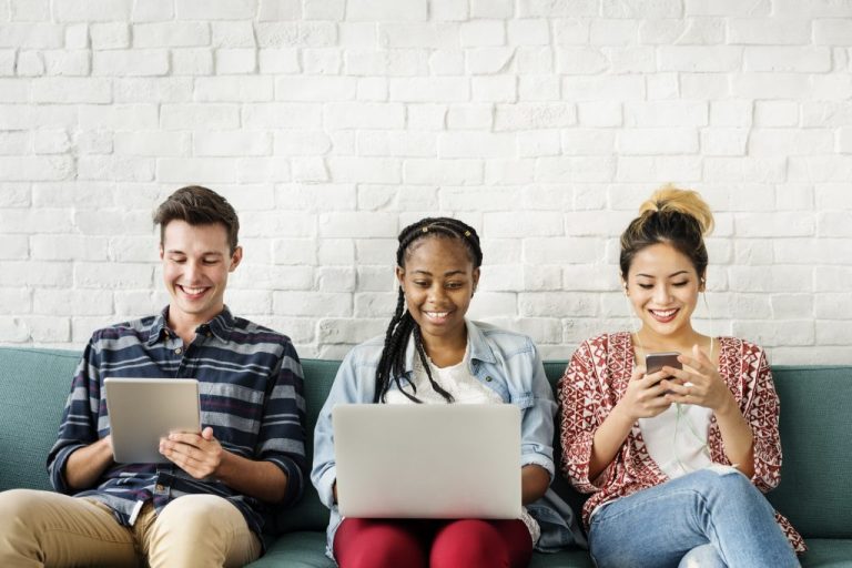 Three teens sitting on sofa looking at devices.