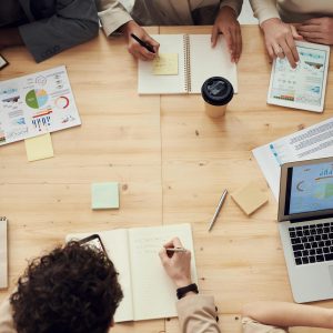 Group of people sitting around a table with notebooks and laptops