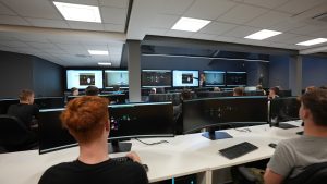 Learners looking at the screen in the Control Room. Teacher at the front of the class