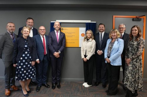 Two groups of people standing either side of yellow and white plaque at the opening of Shell Hub.