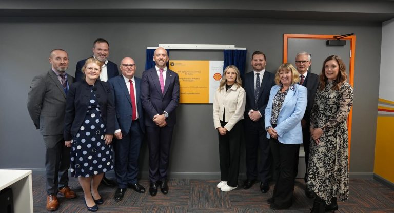Two groups of people standing either side of yellow and white plaque at the opening of Shell Hub.