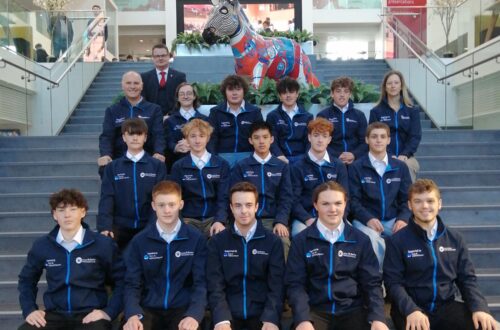Group of learners sat on stairs with colourful donkey statue in background.