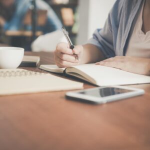 someone sitting at a desk completing a course. Notepad, coffee cup and phone in front of them