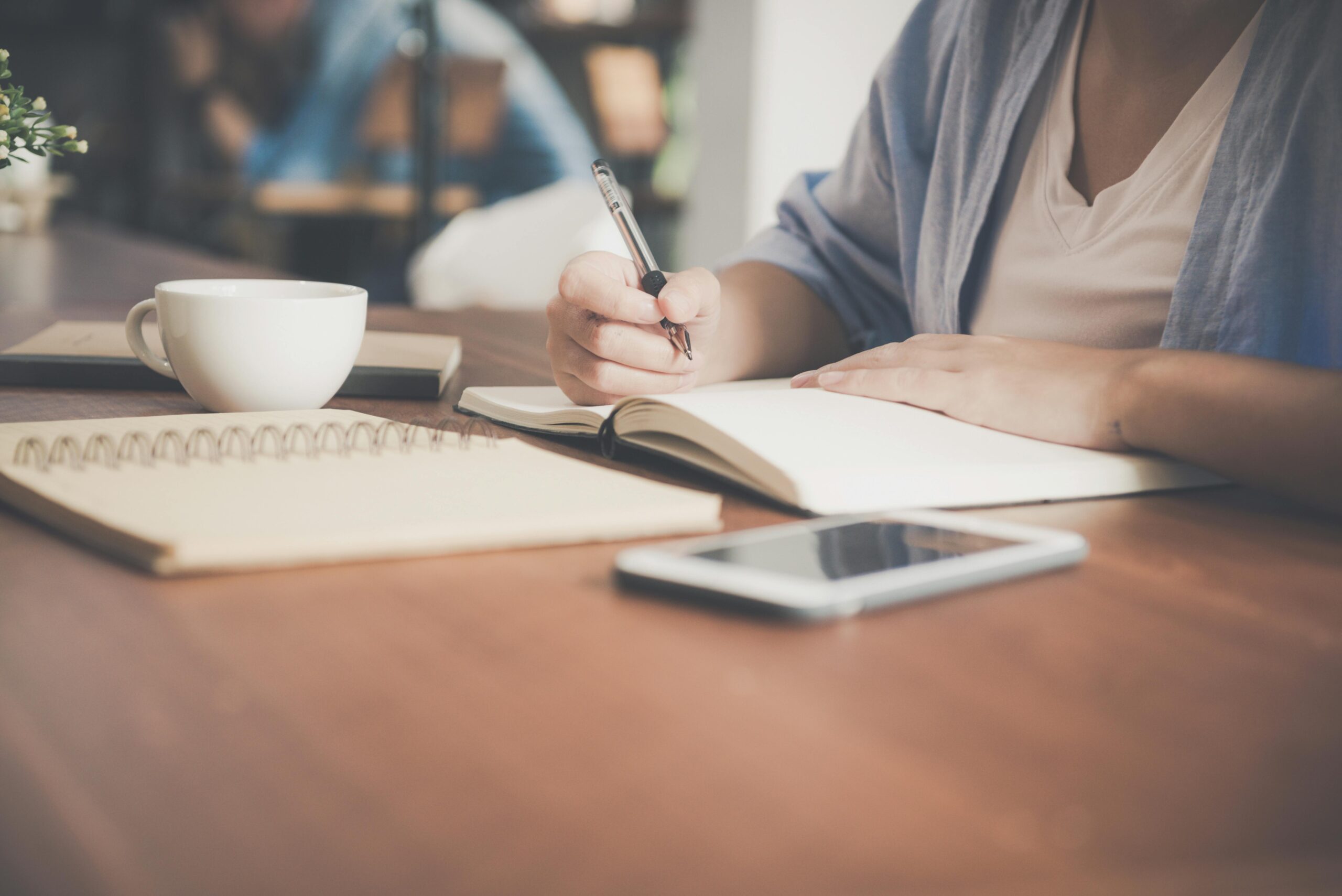 someone sitting at a desk completing a course. Notepad, coffee cup and phone in front of them