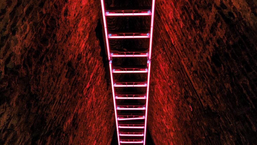 A vertical shot of a pink neon staircase in a cave