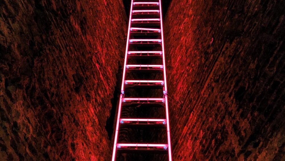 A vertical shot of a pink neon staircase in a cave
