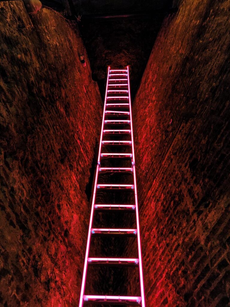 A vertical shot of a pink neon staircase in a cave