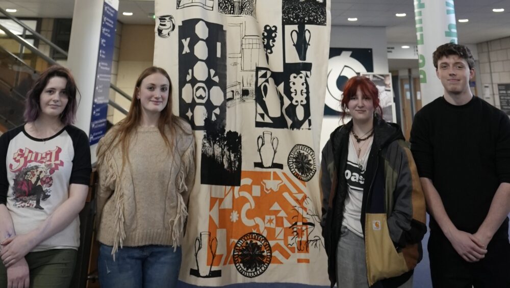 Four Art learners stood in front of large banner