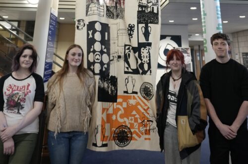 Four Art learners stood in front of large banner
