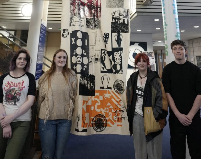 Four Art learners stood in front of large banner
