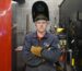 Luke with arms folded located in a welding booth wearing his visor