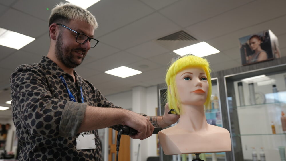 Marcus styling a mannequin head with bright yellow hair