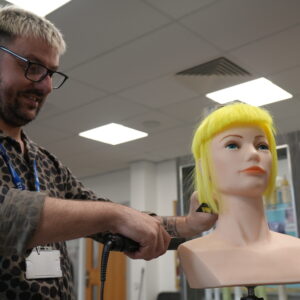 Marcus styling a mannequin head with bright yellow hair