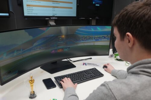 Back of student sitting at wide screen playing Esport game.