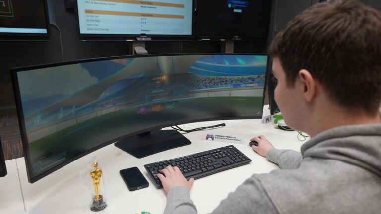 Back of student sitting at wide screen playing Esport game.