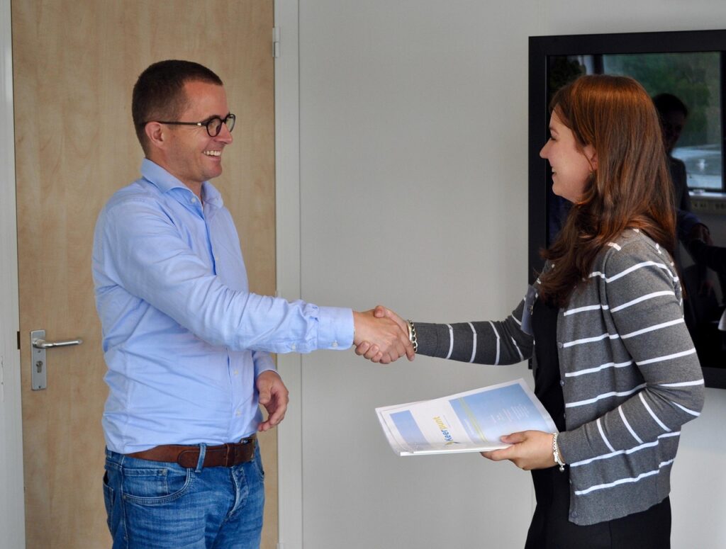2 people shaking hands while holding paperwork