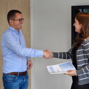 2 people shaking hands while holding paperwork