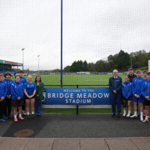 Students and staff stood in front of the Bridge Meadow sign on the Haverfordwest AFC pitch