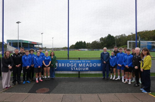 Students and staff stood in front of the Bridge Meadow sign on the Haverfordwest AFC pitch