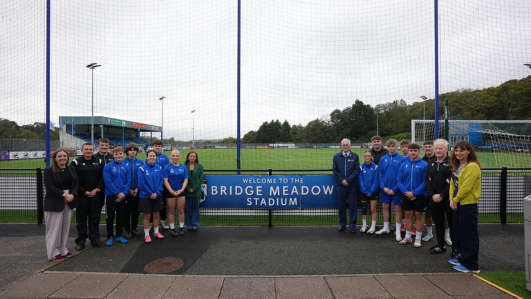 Students and staff stood in front of the Bridge Meadow sign on the Haverfordwest AFC pitch