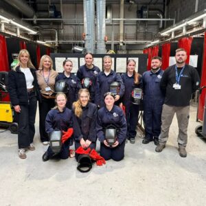 Group photo students and staff in welding workshop.