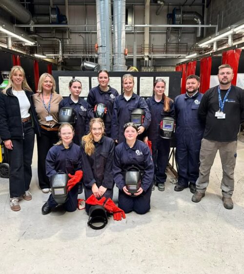 Group photo students and staff in welding workshop.