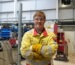 Student wearing yellow overalls with arms crossed in a workshop.