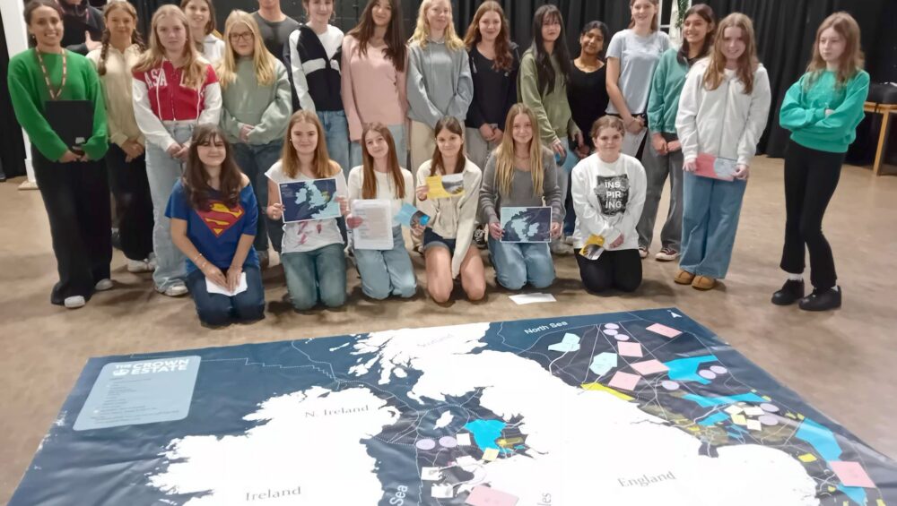 Group of students and staff standing behind a map of the UK on the floor.