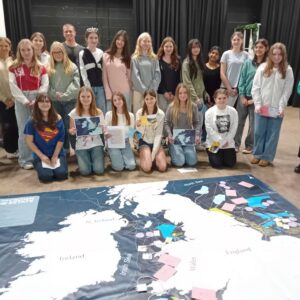 Group of students and staff standing behind a map of the UK on the floor.