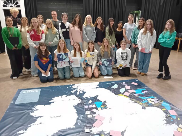 Group of students and staff standing behind a map of the UK on the floor.
