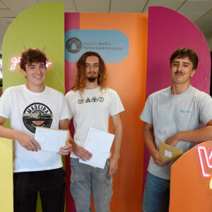 Three students standing in front of bright stands holding results.