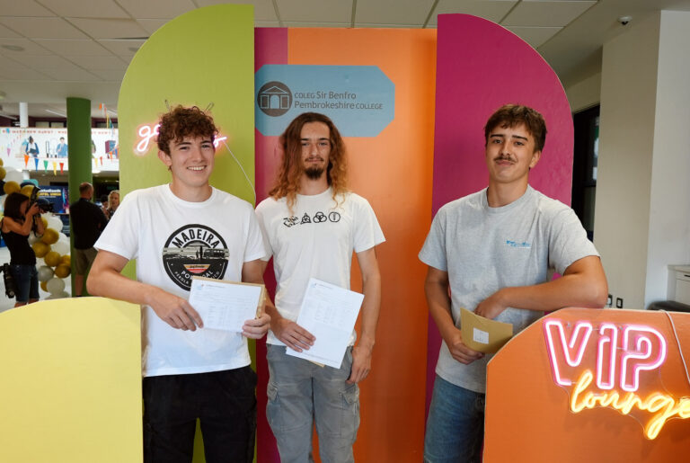 Three students standing in front of bright stands holding results.