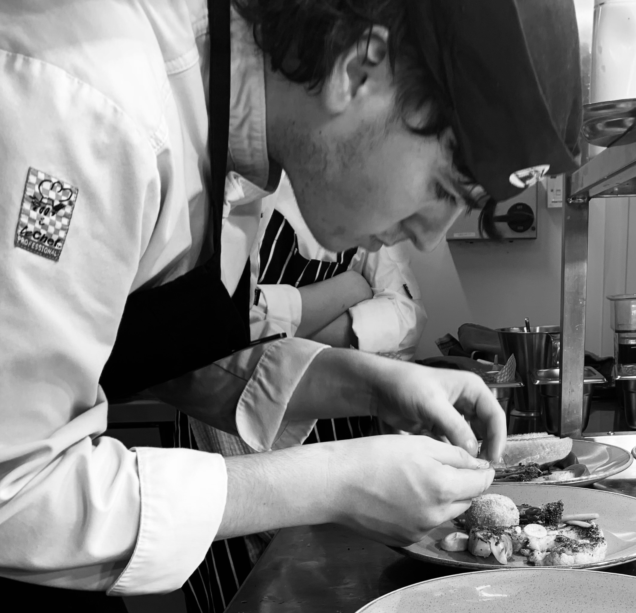 Black and white image of a student chef doing fine work on plating.