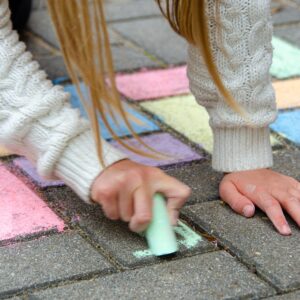 child's hand drawing with chalk on a pavement
