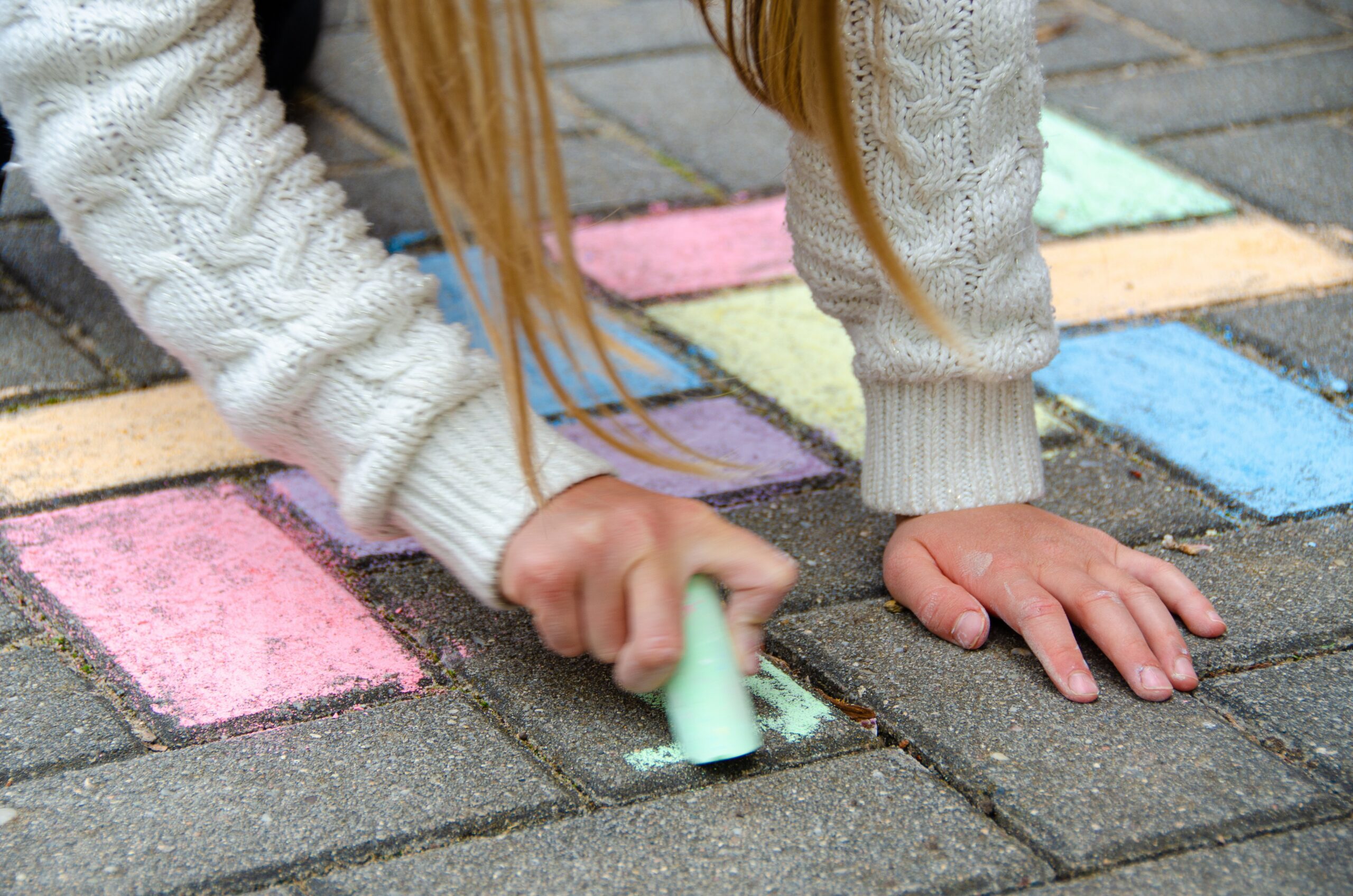 child's hand drawing with chalk on a pavement