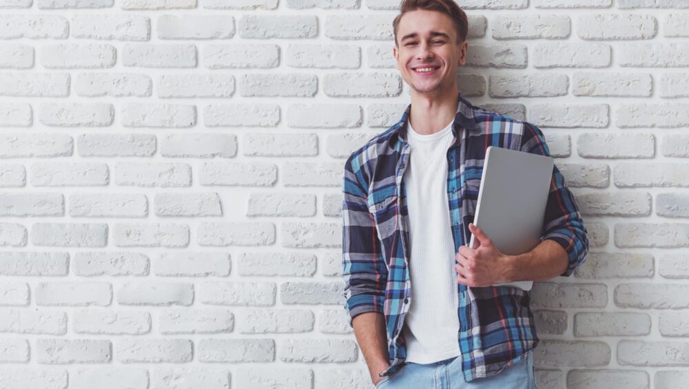 leanerner standing against a wall holding a laptop