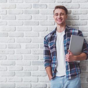 leanerner standing against a wall holding a laptop